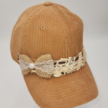 Load image into Gallery viewer, A tan corduroy baseball cap featuring a decorative band with a burlap bow, white lace, and a small pearl accent on the brim, set against a plain light gray background.