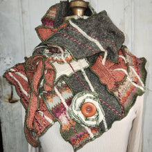 Load image into Gallery viewer, A handmade, multi-colored patchwork knit scarf with a large brown button, displayed on a white ribbed sweater dress form against a rustic white wooden background.