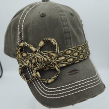 Load image into Gallery viewer, An olive green distressed baseball cap with white contrast stitching, featuring a decorative gold and black patterned headband with a large flower embellishment on the side, displayed on a white mannequin head.