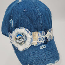 Load image into Gallery viewer, A distressed blue denim baseball cap featuring a decorative band around the middle with a white and blue patterned fabric, a faux fur trim, and a round Busch Lights bottle cap badge.
