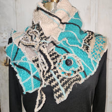 Load image into Gallery viewer, A handmade, multi-layered crochet scarf draped on a black mannequin torso against a white wooden door background. The scarf features turquoise, beige, black, and gray yarn patterns with a decorative button.
