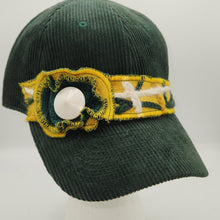 Load image into Gallery viewer, A dark green corduroy baseball cap with a decorative yellow and white embroidered band around the crown, featuring a white snap button on the front, displayed on a white mannequin head against a light gray background.
